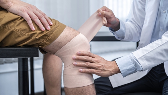 Doctor wrapping knee in guaze